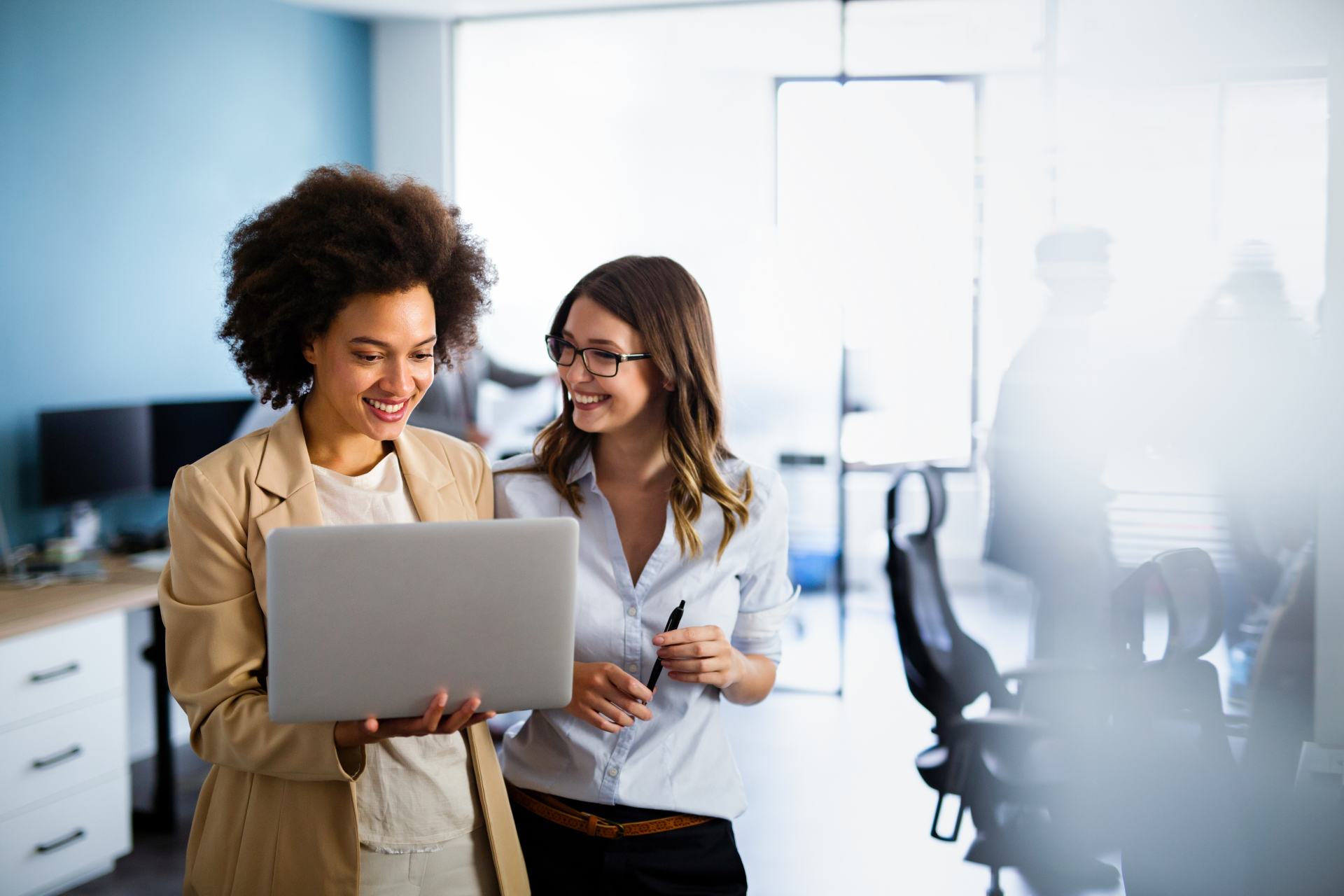 Fröhliche Geschäftsfrauen, die in einem Firmenbüro gemeinsam online am Laptop arbeiten.