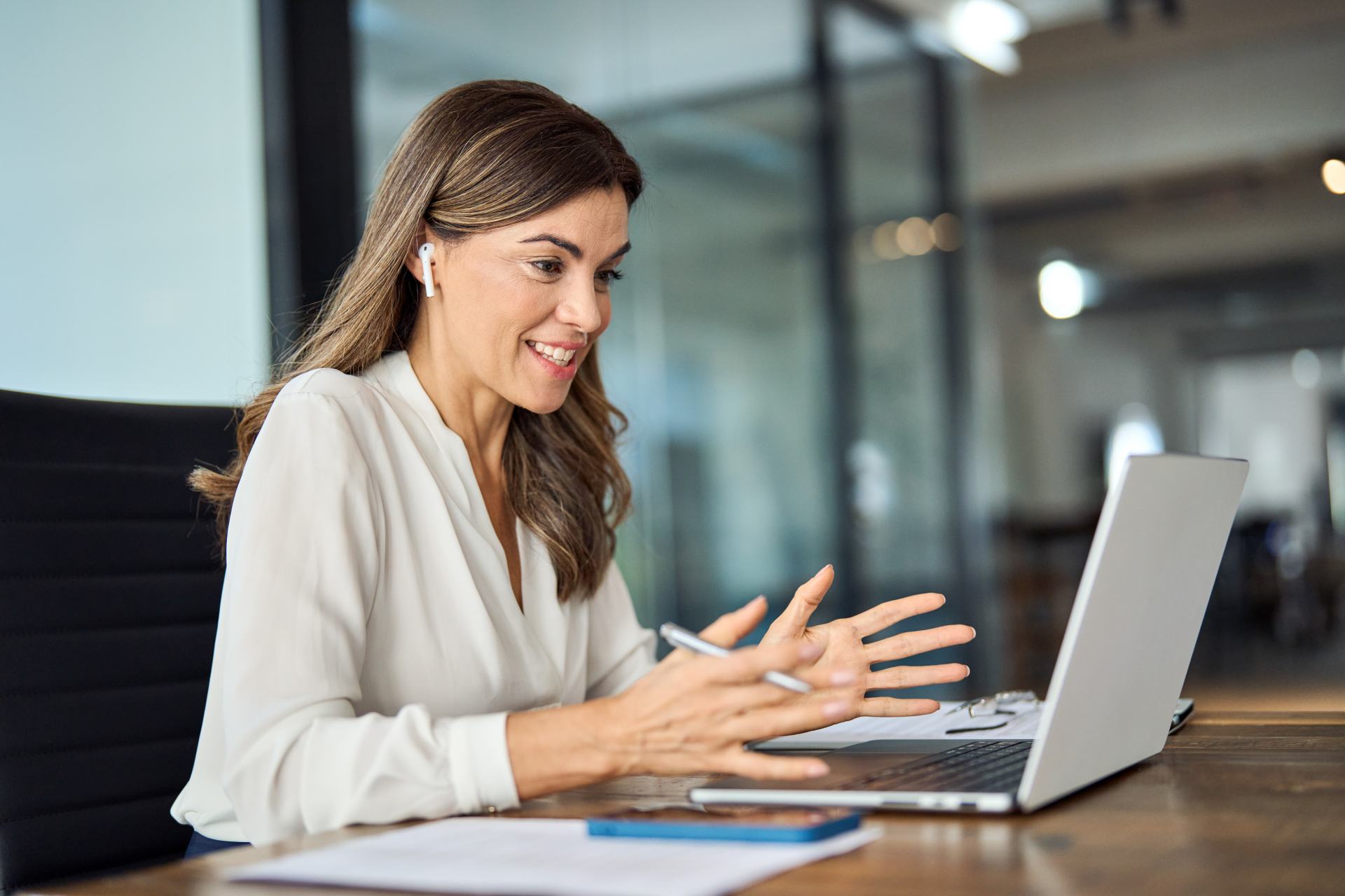 Fröhliche professionelle Frau im HR-Bereich / lächelnde, reife Geschäftsfrau im Büro, die einen Laptop-Computer mit hybrider Besprechung oder Remote-Bewerbungsgespräch ansieht.