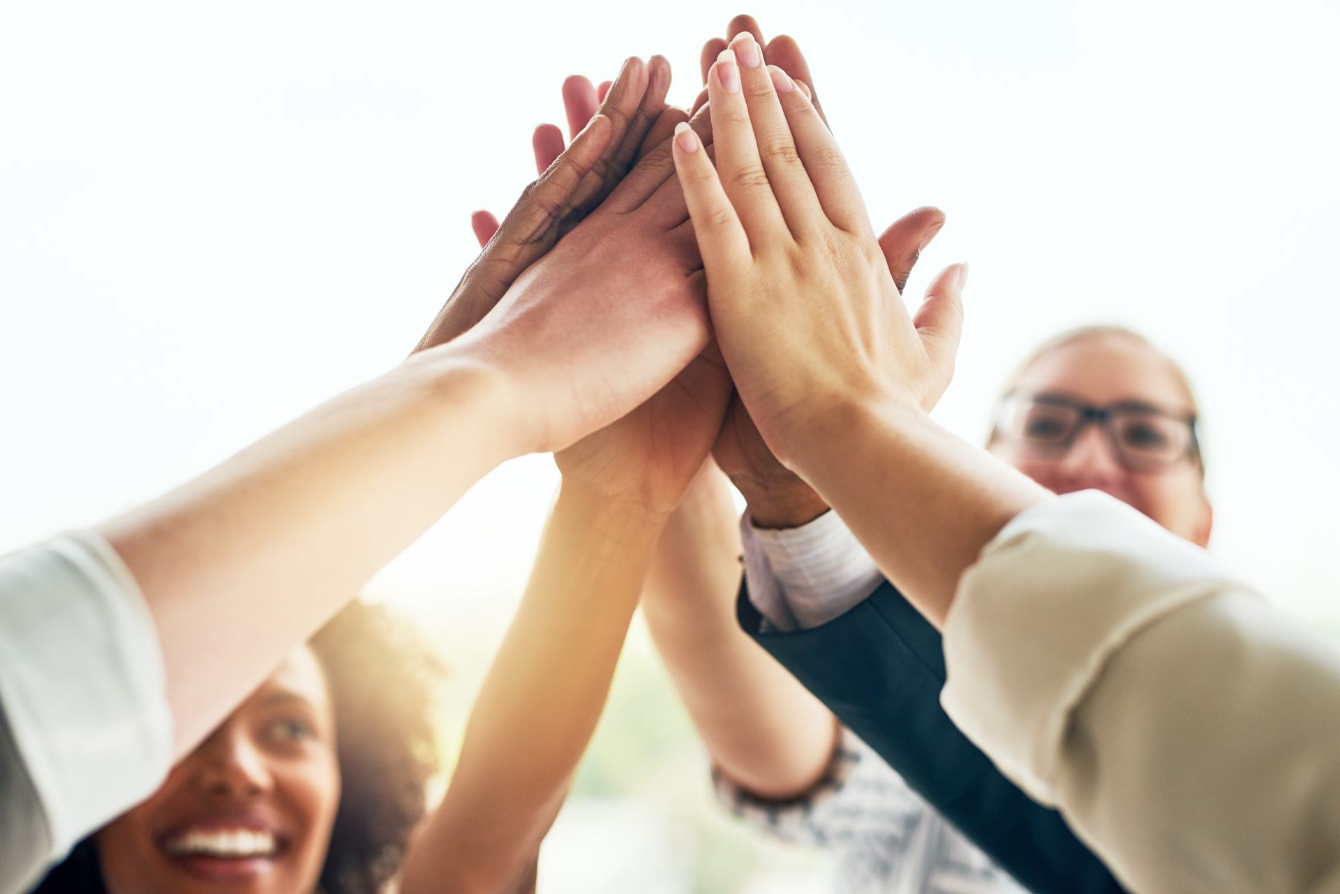 Geschäftsleute und Mitarbeiter freuen sich im Büro mit einem High Five über die Zusammenarbeit, Teamarbeit und den Zusammenhalt bei einem Projekt. Mitarbeiter zeigen Solidarität und lächeln, während sie sich im Team zusammenschließen, um gemeinsam zu arbeiten – begleitet von Feierlichkeiten und gegenseitiger Unterstützung.
