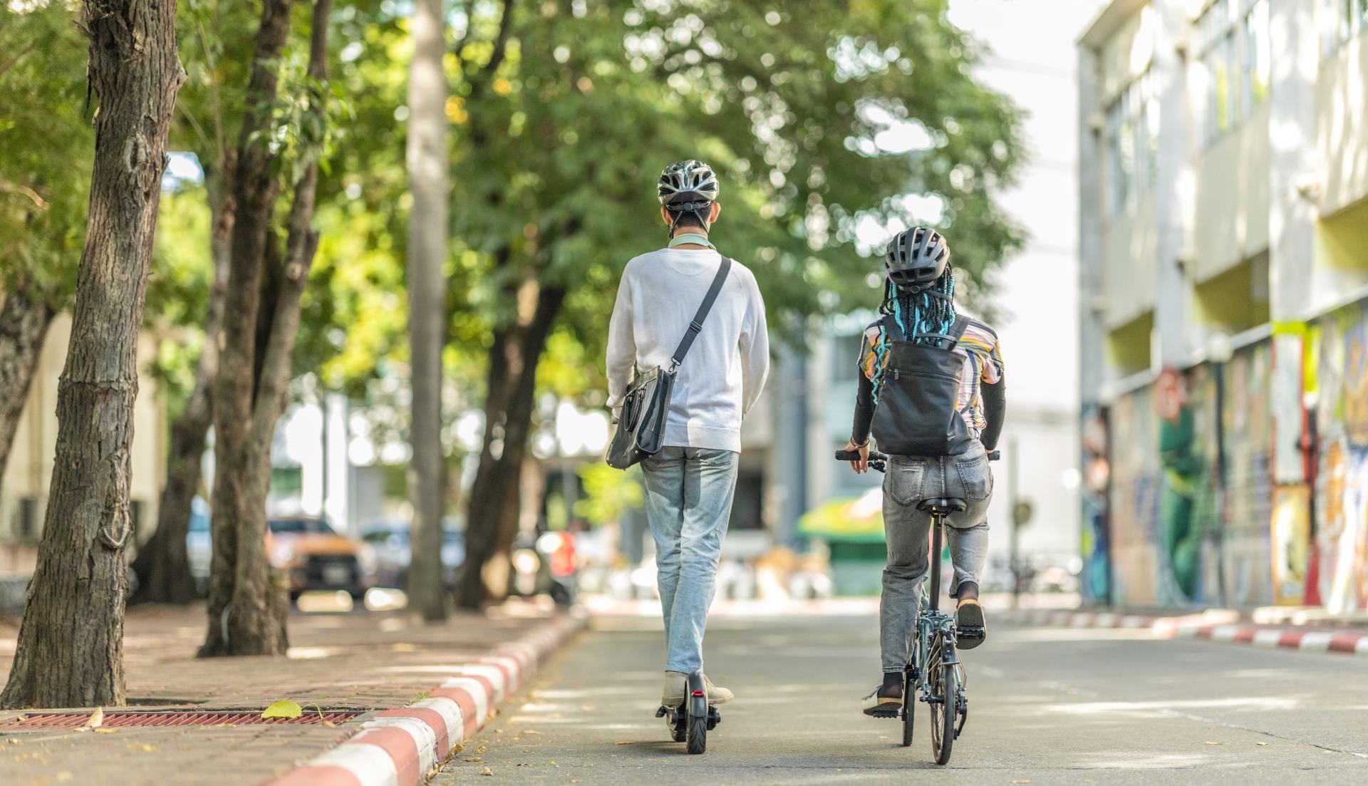 Zwei junge Menschen, die mit umweltfreundlichen Verkehrsmitteln, Elektroroller und Klapprad, unterwegs sind.