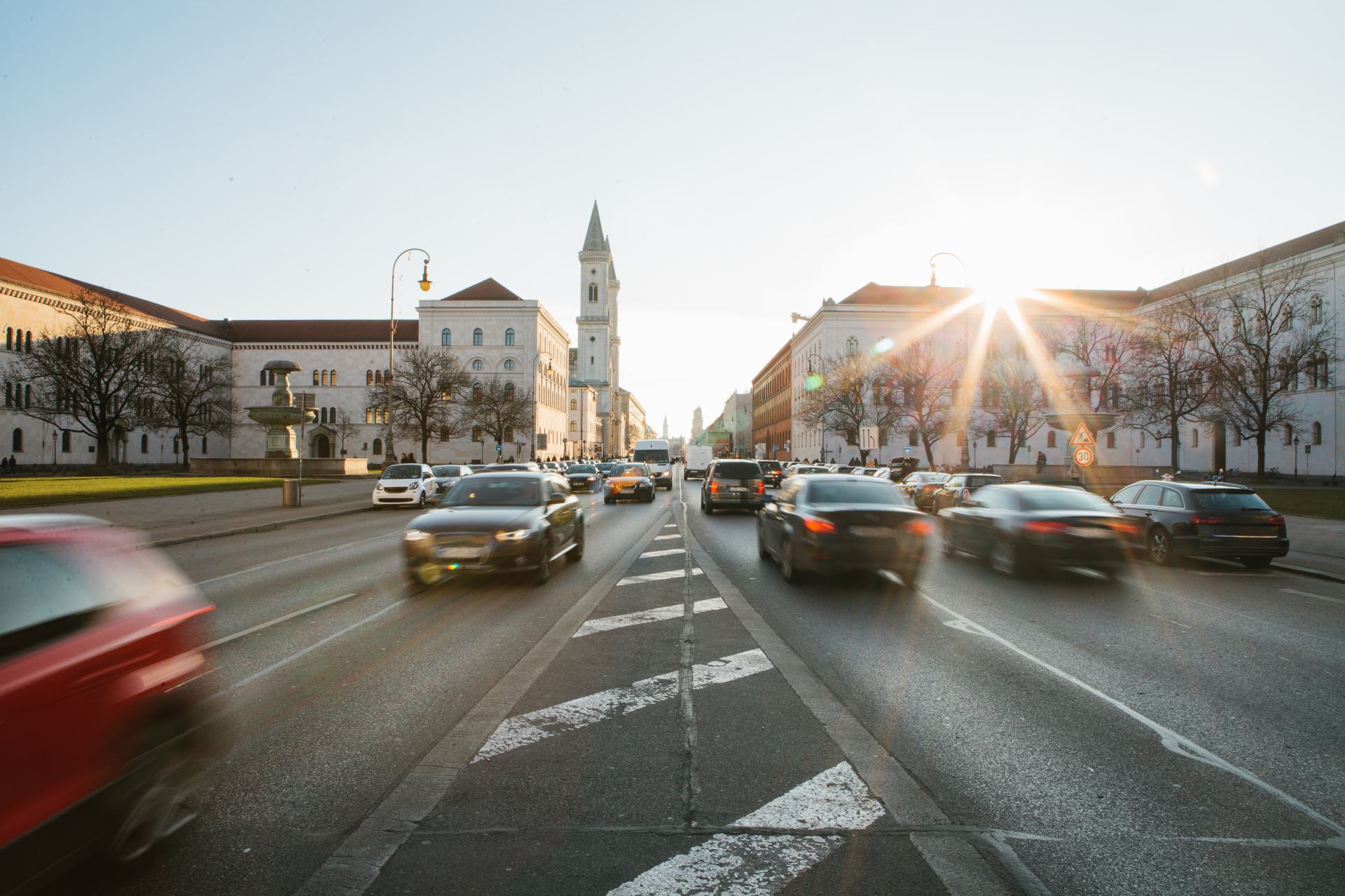 Blick auf die Leopoldstraße in München. Ein schnell vorbeirauschendes Auto vor dem Hintergrund des Sonnenuntergangs.